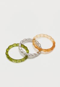 Τρία στρογγυλά, υφασμένα δαχτυλίδια σε πράσινο, ασημί και κεχριμπαρένιο χρώμα, τοποθετημένα το ένα επάνω στο άλλο σε λευκό φόντο.