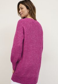 Magenta striktrøje med en løs pasform, lange ærmer og en bred udskæring. Blød tekstur og en let oversized silhuet.