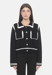 Cardigan corto navy con cuciture bianche a contrasto, grandi tasche frontali e bottoni argentati. Presenta maniche lunghe e tessuto a maglia testurizzato.
