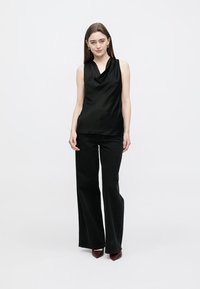 Black sleeveless top with a cowl neckline, paired with wide-leg black trousers and maroon heels, set against a plain white background.