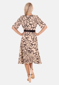 Beiges Kleid mit schwarzem Blumenmuster, knielang, kurze Puffärmel, tailliert mit einem schwarzen Gürtel, ausgestellter Rock, glatte Stofftextur.