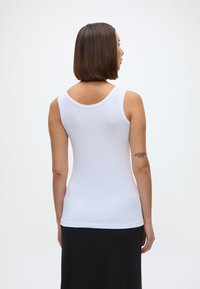 Baltas bezpiedurkņu tops ar noapaļotu izgriezumu, piegulošs dizains un mīksta tekstūra, apvienots ar melnu svārku.