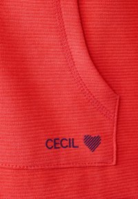 Tessuto rosso testurizzato con dettaglio della tasca, caratterizzato da un logo "CECIL" blu navy e un design a cuore a righe.