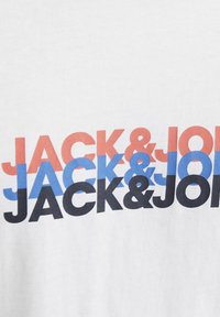 Witte katoen t-shirt met herhaalde tekst "JACK & JONES" in rood, blauw en zwart. Vetgedrukt lettertype met variërende kleuren creëert visueel contrast.