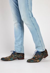 Multikleurige patroon schoenen met decoratieve kronkel ontwerpen, zwarte stof, blauwe veters en een lage bruine hak, gecombineerd met lichte spijkerbroeken.