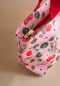 Růžová květinová taška s červenými uchy, se zipovým uzávěrem a zlatými detaily. Vyznačuje se vzory třešní a květin na růžovém pozadí.