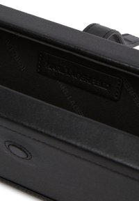 Wnętrze czarnej skórzanej torby o gładkiej fakturze, z metką wszytą w podszewkę z tkaniny oraz okrąłym detalem metalowym po boku.