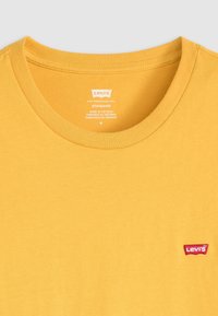 Geel Levi's T-shirt met ronde hals, rode Levi's logo-tag op de borst en bedrukte maat- en productiedetails aan de binnenkant van de kraag.