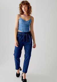 Top in denim con spalline sottili, abbinato a pantaloni in denim blu a vita alta. Presenta una cintura annodata e gambe tapered. Tacchi neri completano il look.