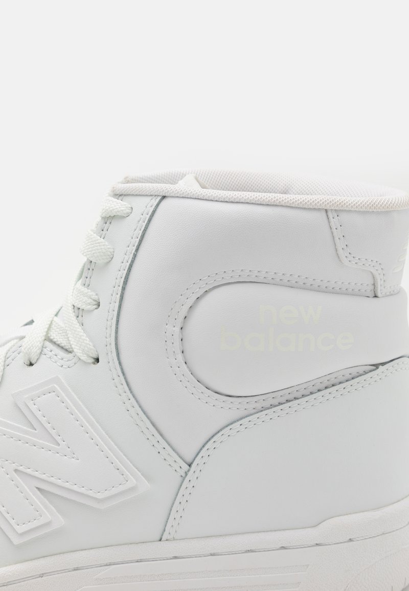 Sneaker alta bianca in pelle sintetica con dettagli testurizzati, caratterizzata da un logo prominente e un design con lacci. Fodera interna morbida.