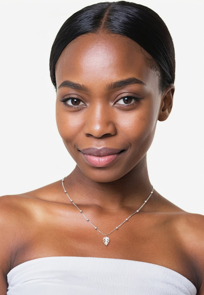 Silverhalsband med ett löv hänge, med små pärlor längs en delikat kedja. Modellen har en jämn hy och ett neutralt uttryck.