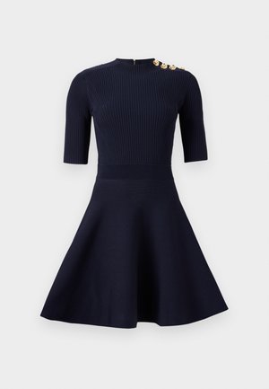 Navyblaues Kleid mit einem figurbetonten, gerippten Oberteil und einem ausgestellt Rock. Es hat kurze Ärmel, einen hohen Hals und goldene Knopfakzente an der Schulter.