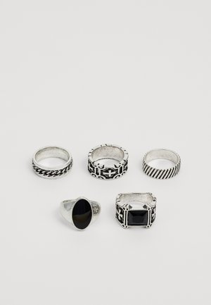 Päť strieborných prsteňov vystavených, so rôznymi dizajnmi: jeden s reťazovým vzorom, ostatné so vyrytými alebo zdobenými akcentmi a dva s čiernymi kameňmi.