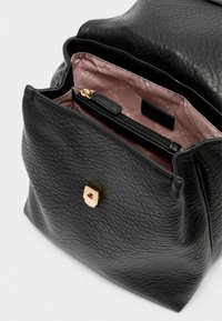 Schwarze Tasche aus strukturiertem Leder mit einem goldfarbenen Verschluss. Das Innere ist mit einem rosafarbenen Futter und einem Reißverschlussfach ausgestattet.