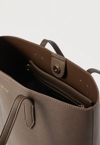 Barna bőrből készült tote táska két fogantyúval, nyitott tetejű, belül cipzáras zsebbel, amelyen arany betűkkel az "Anna Field" márkanév olvasható.