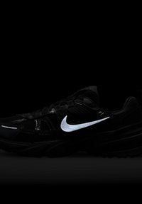 Crne atletske tenisice s mrežastim gornjim dijelom, podstavljenim ovratnikom i gumeni potplat. Sadrže istaknuti reflektirajući srebrni Nike znak i teksturirane detalje.