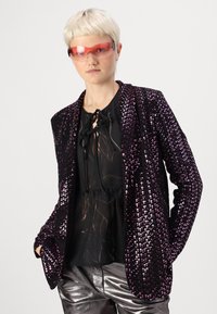 Blazer noir à paillettes pour femmes avec des accents roses, présentant une coupe décontractée et une texture brillante, superposé sur un haut noir et un pantalon argenté.
