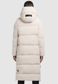 Long, white, puffer coat with a hood, featuring horizontal quilting, a logo tag on the back, and zippered accents on the sides.