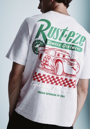 Persona che indossa una maglietta grigia con "Rust-eze Bumper Ointment" verde e rosso e grafica di un’auto da corsa rossa di Lightning McQueen sulla schiena.