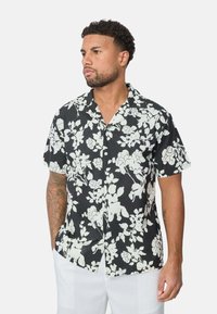 Chemise noire à manches courtes avec un motif floral blanc ; col standard, fermeture à boutons, tissu léger et coupe décontractée.