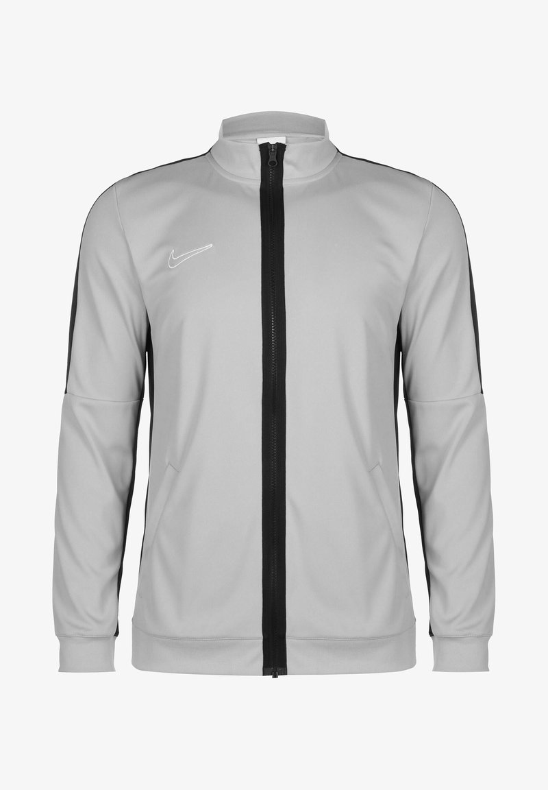 Giacca zip-up grigio chiaro con strisce laterali nere, colletto alto e logo Nike bianco. Realizzata in tessuto liscio e flessibile con una vestibilità strutturata.