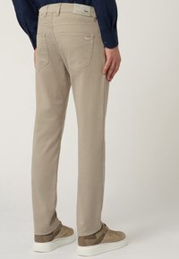 Beige chinos met een rechte pijpdesign, voorzien van achterzakken en een subtiele merktag. De stof lijkt soepel met een nette afwerking.