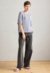 Maglione grigio chiaro a maniche corte, indossato con pantaloni larghi grigi scuri e sandali viola pastello con una suola testurizzata.