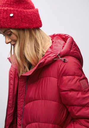 Giacca a vento rossa con cappuccio texturizzato, dotata di chiusura con zip e dettagli con cordino. Il materiale appare lucido e isolato.