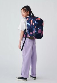 Marineblauem Rucksack mit pinken und blauen kreisförmigen Mustern, mehreren Fächern und verstellbaren Trägern. Wird von einer Person in lässiger Kleidung getragen.