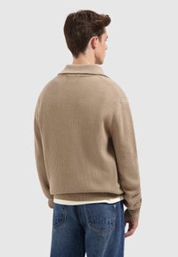 Beige geribbelde trui met een brede kraag, ontspannen pasvorm en lange mouwen, gecombineerd met donkerblauwe denim jeans.