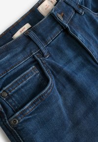 Slim fit denim jeans in een donkere blauwe wassingen, met een gladde textuur, contrasterende bruine stiksels, twee voorzakken en een metalen knoopsluiting.