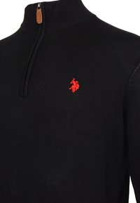 Schwarzer Pulli mit hohem Kragen, versehen mit einem roten gestickten Polo-Spieler-Logo auf der linken Brust und einem braunen Reißverschluss-Zipper.
