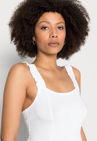 Top branco sem mangas com alças texturizadas e franzidas, design ajustado e tecido suave. Corte simples com uma estética suave e minimalista.