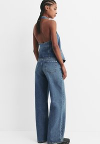 Denim halter top z odprtim hrbtom, v kombinaciji s širokimi hlačami. Svetlo modra pranja, teksturiran material, ki vključuje zadnje žepe z okrasnimi elementi.