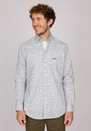 Chemise boutonnée bleu clair avec un motif floral en jaune et marine. Manches longues, col, et un petit logo sur la poitrine. Matière en coton.