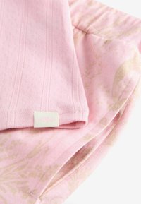 Vêtements pour bébé de couleur rose doux avec des motifs floraux, fabriqués dans un tissu tricoté texturé, avec une petite étiquette en tissu arborant un design floral.