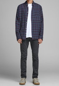 Košile z pruhované flanelové látky v námořnické modři, červené a bílé; bílá trička s kulatým výstřihem; tmavé džíny; světlé tenisky s texturovanými podrážkami.