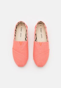 Korallenfarbene Canvas-Slipper mit strukturierter Oberfläche, ausgestattet mit einem V-förmigen Ausschnitt an der Vorderseite und einer gestreiften Innensohle. Hersteller: TOMS.