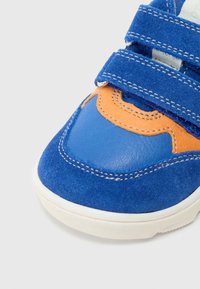 Παιδικό αθλητικό παπούτσι σε μπλε και πορτοκαλί χρώμα με δύο μπλε λουριά βέλκρο και λευκή σόλα, εμφανιζόμενο από μπροστά σε λευκό φόντο.