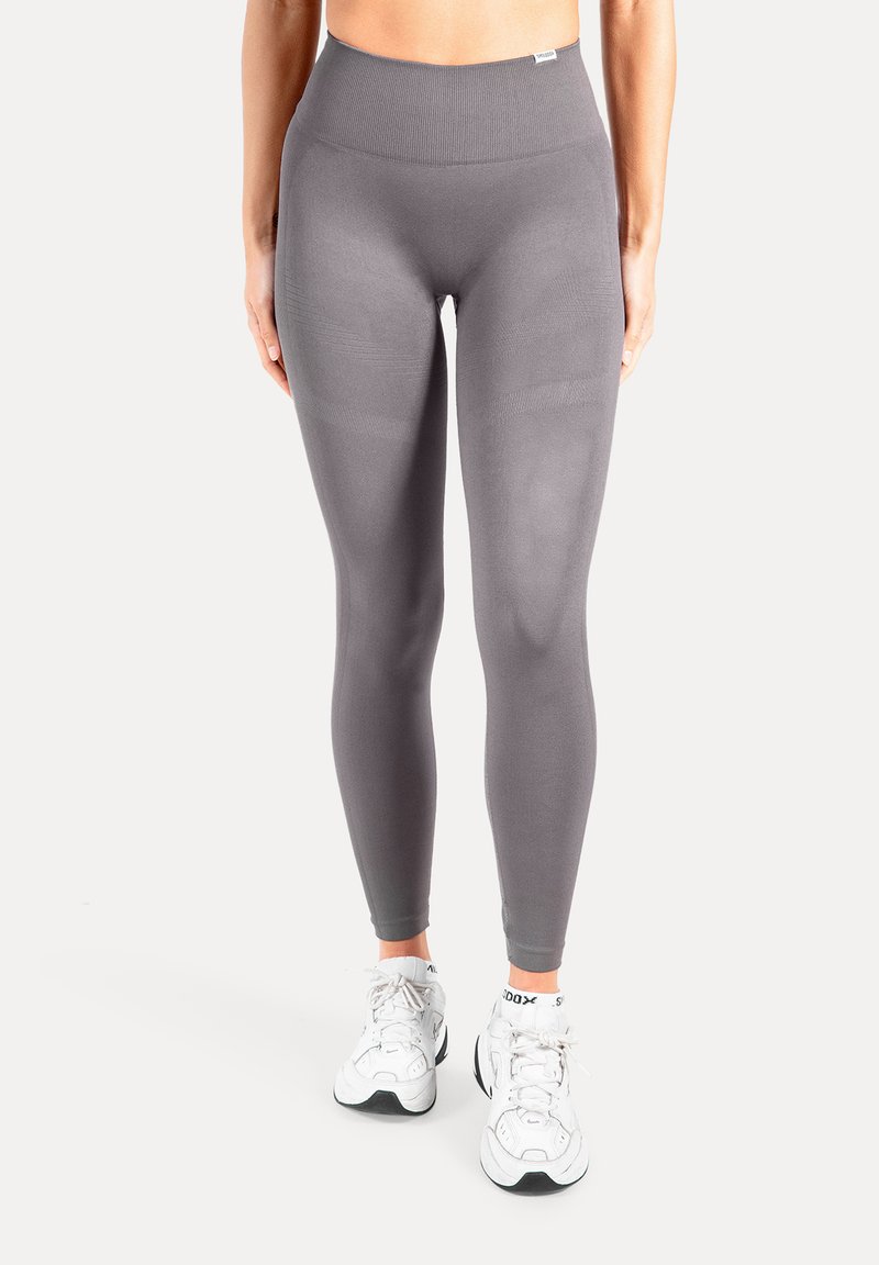 Leggings taille haute gris en tissu extensible, avec une texture lisse et une coupe ajustée, associés à des baskets blanches.