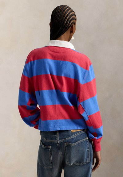Πουλόβερ με κόκκινες και μπλε ρίγες, λευκό γιακά, μακριά μανίκια και άνετη εφαρμογή. Η πίσω όψη δείχνει διακοσμητική ραφή και μανσέτες.