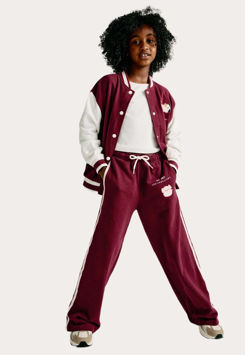 Bordový univerzitní svetr s bílými rukávy, bílý tričko, ladící bordové tepláky s bočními pruhy a grafikou a béžové tenisky.