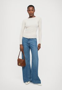 Ribbed cream long-sleeve top paired with wide-leg blue jeans, holding a brown shoulder bag and wearing white pointed-toe heels.