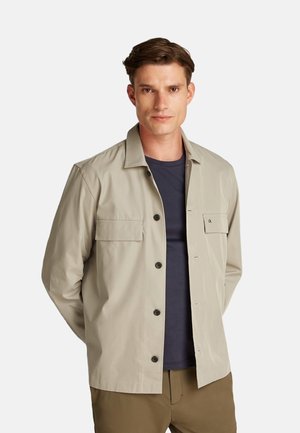 Giacca beige chiaro dal design elegante, con chiusura a bottone, due tasche frontali e un logo discreto sul petto. Tessuto leggero.