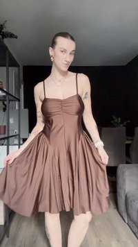Robe en satin marron avec un corsage ajusté, devant froncé, fines bretelles et une jupe fluide. Comprend des plis subtils et une texture lisse.