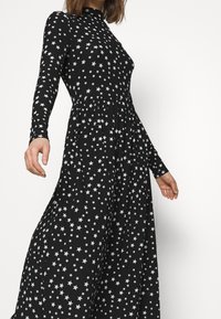 Svart långärmad klänning med en åtsittande body och utsvängd kjol, prydd med silverstjärnor över hela. Slätt, lätt tyg.