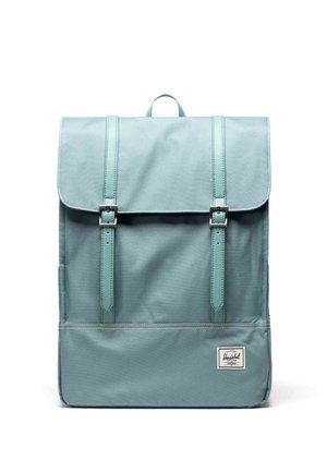 Petrolejový batoh z hladkej látky, s preklápacou chlopňou, dvoma nastaviteľnými remienkami a logovou nášivkou na spodnej časti.