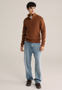 Rudas megztinis su pusiau apykakle ir dviem mygtukais, derinamas su šviesiai mėlynomis plačiomis džinsinėmis kelnių ir tamsiais batais. Paprastas ir kasdienis dizainas.