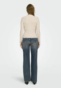 Beige geribbelde top met lange mouwen, gecombineerd met hooghangende, wijde blauwe jeans. De jeans hebben een vervaagde wassing en een klassiek zakontwerp.