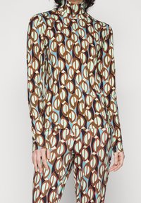 Aansluitende, langwerpige top en bijpassende leggings in een meerkleurig patroon van overlappende ovalen. Kleuren zijn bruin, muntgroen en blauw.